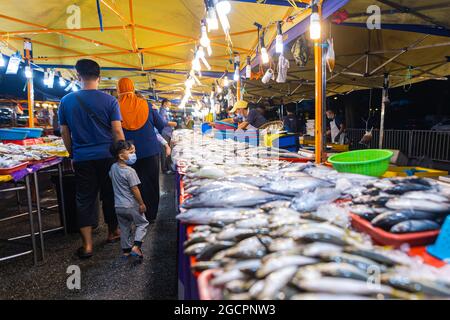 Street food night market at  Putrajaya, near Kuala Lumpur. Seafood stand with fresh fish on the counter. Malay family with a little boy passing by Stock Photo