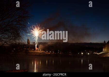 fireworks in the night sky against the backdrop of the city landscape. The sky is hazy, and the lights are reflected in the water Stock Photo