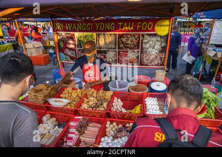 A tofu seller at the street fresh market Putrajaya, Kuala Lumpur. Customers wait for the seller to pack their goods. Man with face mask sells tofu Stock Photo
