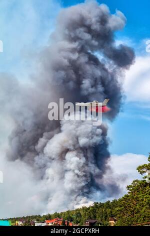 Big amphibious fire aircraft drops water on large forest fire near the village Stock Photo