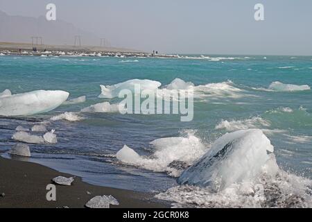 Piece of ice on black sand beach and in the river, river and beach in the background, Diamond Beach, Breidermerkursandur, Iceland Stock Photo