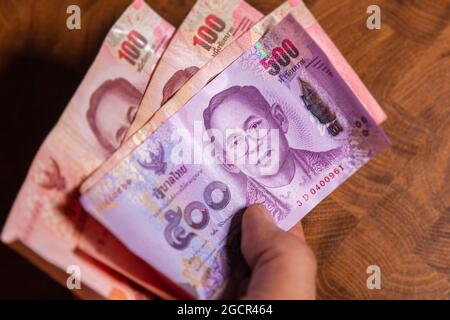 Man hand flip thai baht banknote, the official currency of Thailand. On front side the portrait of the Rama or King,  Close up Paper Money of Thailand Stock Photo