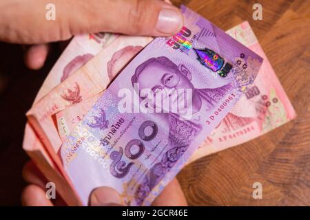 Man hand flip thai baht banknote, the official currency of Thailand. On front side the portrait of the Rama or King,  Close up Paper Money of Thailand Stock Photo