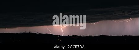 Lightning strikes from behind the clouds in a mountain landscape at night Stock Photo