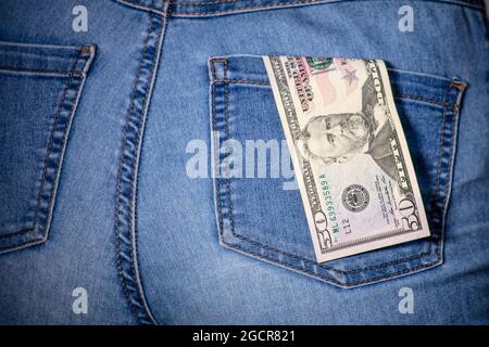 50 dollars in a female jeans pocket. American fifty dollar notes stuck in a woman jeans pocket. Fifty US Dollar hanging in woman jeans. Denim and mone Stock Photo