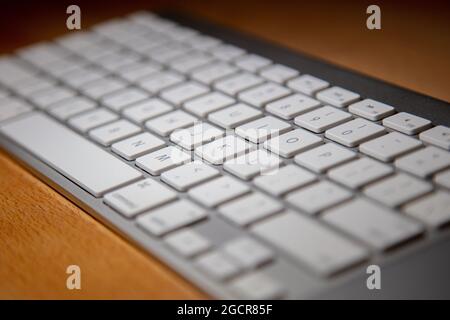 Close up of a white aluminum keyboard on a wooden desk.  Macro photography of a wireless computer keyboard. White keys on a silver frame. Detailed sho Stock Photo