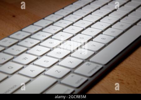 Close up of a white aluminum keyboard on a wooden desk.  Macro photography of a wireless computer keyboard. White keys on a silver frame. Detailed sho Stock Photo