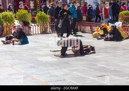 Lhasa, Tibet, China - November 15, 2019:  Tibetan  woman prays on her knees in front of the Jokhang Temple.  Sliding on the floor on the knees for hou Stock Photo