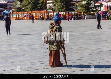 Lhasa, Tibet, China - November 15, 2019: Old Tibetan woman  on  crutches on the Jokhang Temple Square.  Poor looking elderly woman in traditional Tibe Stock Photo