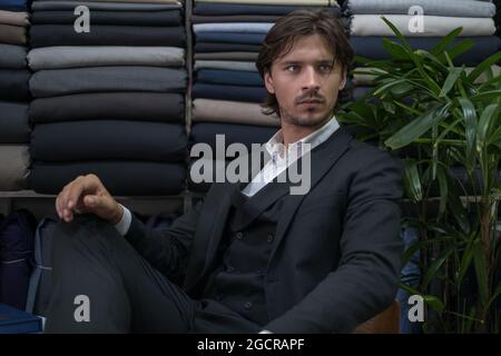 Handsome man in black suit sitting in atelier and looking aside. Serious eyes. High quality photo Stock Photo