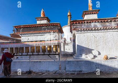 Lhasa, Tibet, China - November 15, 2019:  Old Tibetan woman walks past prayer drums and touches the drum with her right hand. Ancient traditional pray Stock Photo