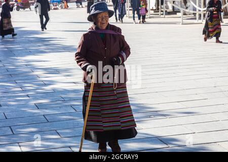 Lhasa, Tibet, China - November 15, 2019: Old Tibetan woman  on  crutches on the Jokhang Temple Square.  Poor looking elderly woman in traditional Tibe Stock Photo