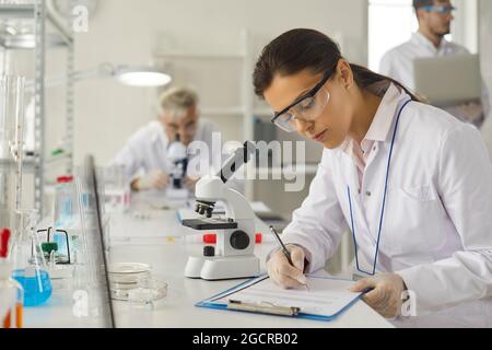 Young woman scientist making notes in report working at chemistry laboratory Stock Photo