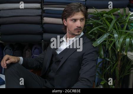 Business man in black suit sitting in atelier and looking aside. Serious eyes. Fabric shop. High quality photo Stock Photo