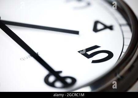 A Modern white wall clock with aluminium frame. Close up to a wall clock, the pointers at half pass 4. Selective focus on the number 5 or 5 o'clock. R Stock Photo