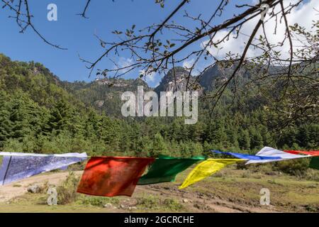 Buddhism Prayer flags waving in the wind on the hiking trail to the tiger nest in Bhutan, Himalaya. Blue sky behind the mountains of Bhutan. Stock Photo