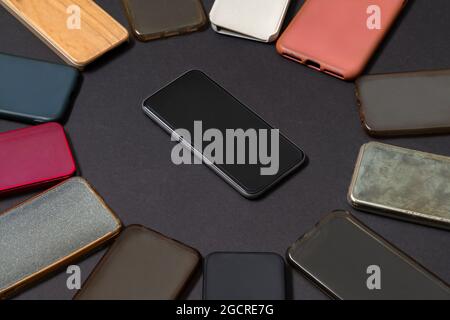 Pile of multicolored plastic back covers for mobile phones on black background with a phone on the side Stock Photo