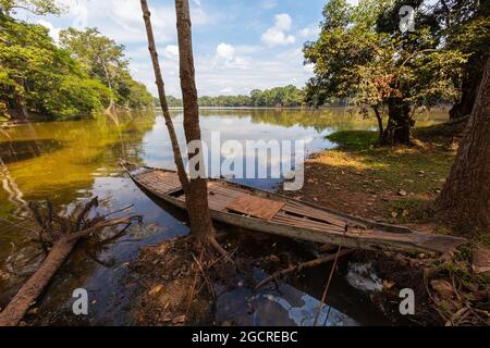 Traditional long tail wooden boat in a small lake near Siem Reap, Cambodia. The sky and the trees around is reflected in the water. Idyllic place just Stock Photo