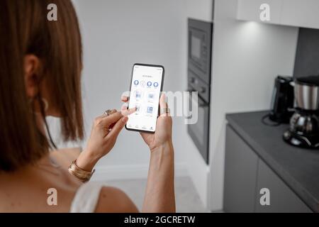 Controlling smart devices with phone on the kitchen Stock Photo
