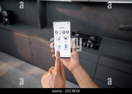 Controlling smart devices with phone on the kitchen Stock Photo