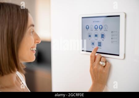 Happy woman controlling smart devices using control panel at kitchen Stock Photo