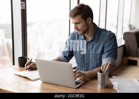 Serious businessman, employee, entrepreneur working at laptop and writing Stock Photo