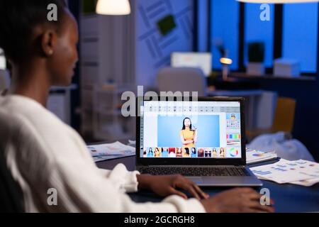 Creative african american retoucher working at design production retouching photography using editing software technology. Photographer on laptop. Woman overworking in creativity office at night Stock Photo