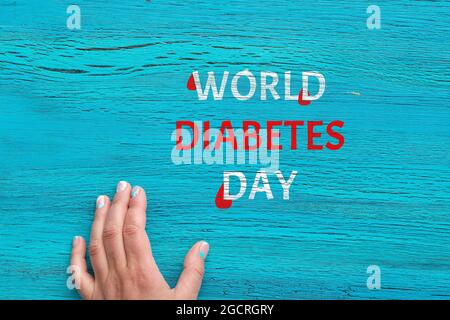 World Diabetes Day, November 14. Text painted white on turquoise painted board with mature woman hand. Drops of blood on the text. Flat lay, top view Stock Photo