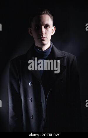 Stylish man in black coat in dark studio Stock Photo