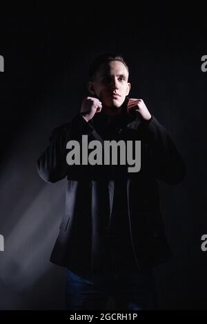 Stylish man in black coat in dark studio Stock Photo