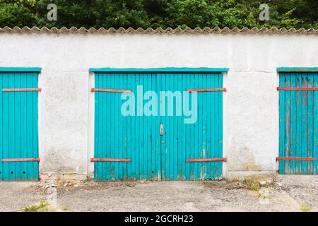 Weathered vibrant turquoise garage doors in  a backyard Stock Photo