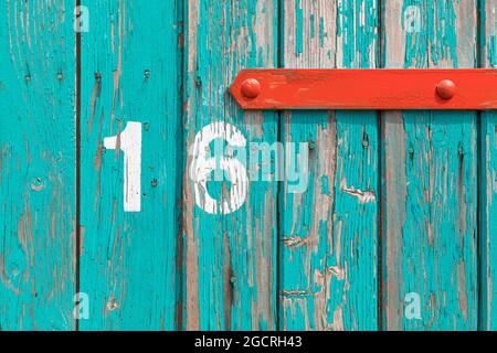 Weathered wooden Turquoise door with red fitting and number 16 abstract background Stock Photo