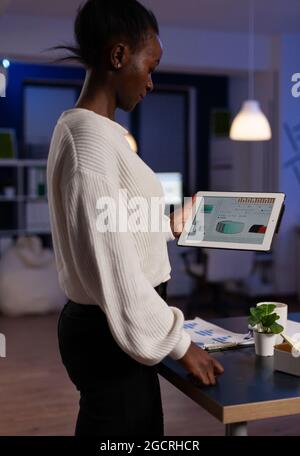 Concentrated african american executive manager holding tablet computer in hands looking at company profit planning financial strategy. Overworked businesswoman working late at night in startup office Stock Photo