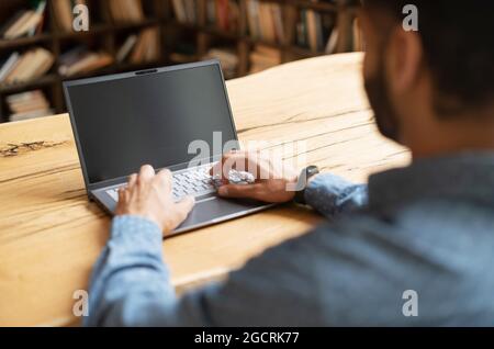 Indian bearded man using laptop with blank screen, using new computer app, back view, copy space for advertising, promotion, copy space Stock Photo