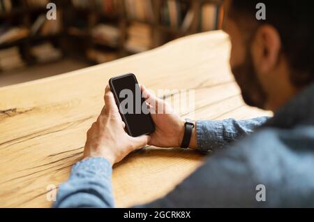 Indian bearded man holding a black mobile phone with blank screen, using new mobile app, male hand with smartphone, back view, copy space for advertising, promotion Stock Photo