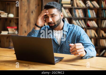 Frustrated Indian freelancer guy staring at the laptop screen with upset face expression, made a mistake with project, was refused a job Stock Photo