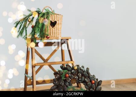 Branch of Christmas tree in wicker basket and wreath of cones with garland. Stock Photo