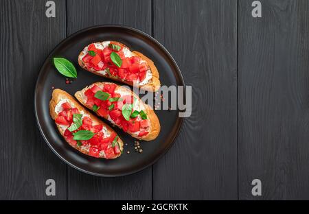 Fried toast with tomatoes, cream cheese and basil on a black background. Stock Photo