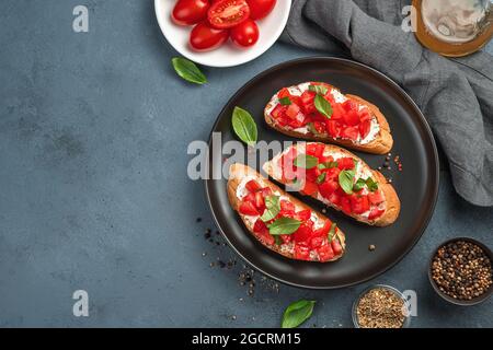 Italian bruschetta with tomatoes, cream cheese and basil on a dark gray-blue background. Stock Photo