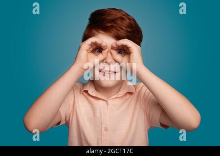 Ginger boy gesturing binocle sign on studio in trendy style. Fashion model. Stock Photo