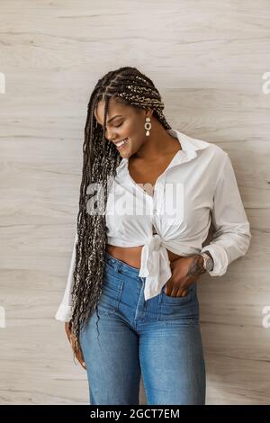 Portrait of a cheerful African American adult woman standing with her arm over her body and looking down to a side. Adult woman with black and yellow Stock Photo