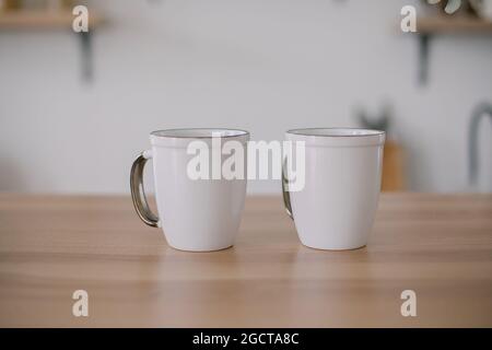 Two white ceramic mugs on wooden kitchen table. Mockup, place for text. Mockup Product Image Stock Photo