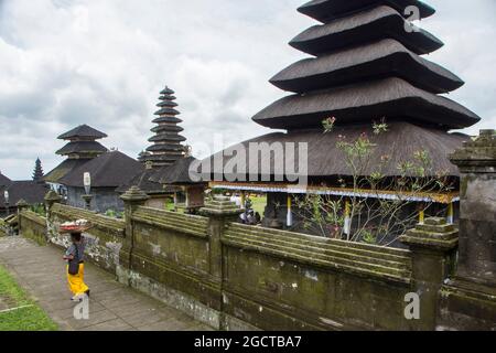 Woman in yellow sarong walking along the wall of the holy Besakih temple. Bali, Indonesia Stock Photo