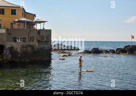 Senior man stand up paddle boarding (SUP) on the shore of the fishing village with a terrace restaurant in the background, Boccadasse, Genoa, Liguria Stock Photo