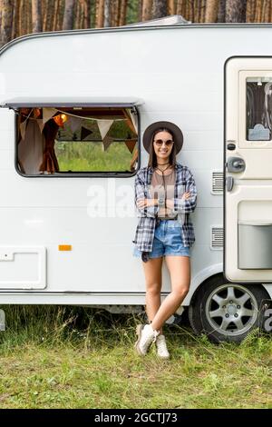 Smiling girl standing by wall of white house on wheels in natural environment Stock Photo