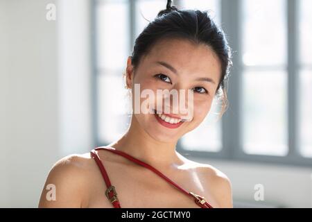 Young Asian girl in a traditional Chinese dress with gathered hair looks at the camera and smiles. Portrait set in an empty building Stock Photo