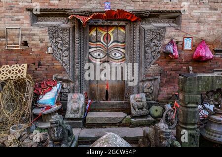 A wooden door with painted Buddha eyes and carved ornaments on a red brick wall, traditional Nepalese architecture in Kathmandu, Nepal Stock Photo