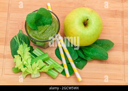 Fresh Green Smoothie of Apple, Celery, and Spinach in Glass Beaker with Yellow Cocktail Straw on Wooden Cutting Board. Vegan Detox Drink. Vegetarian Culture. Healthy Eating and Fruit Diet Stock Photo