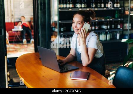 Woman manager talking on the phone while sitting in a cafe with a laptop, business negotiations. Stock Photo
