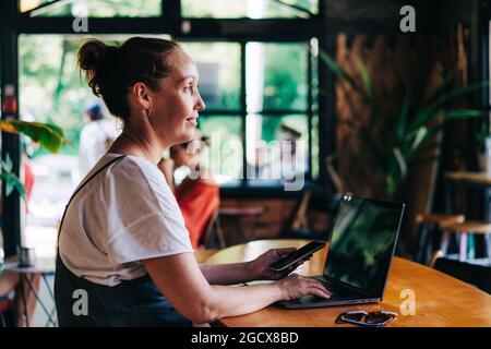 Cute inspired woman working remotely from a cozy cafe on a laptop using wireless technologies. Stock Photo